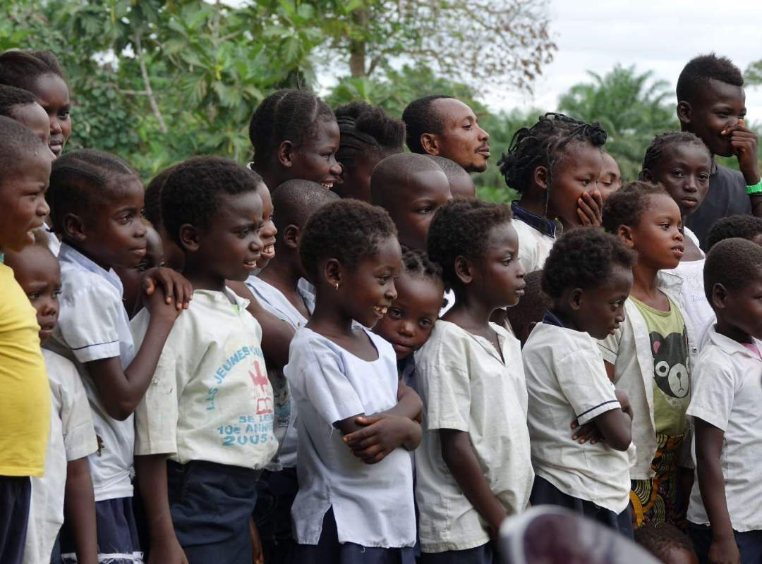 Groep kinderen kijkt nieuwsgierig naar het educatief toneel op het eiland Mbiye.